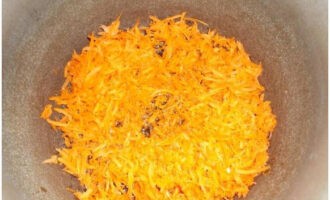 Приступим к приготовлению солянки с капустой и помидорами на зиму в банках. Натираем морковь на крупной терке и жарим ее до мягкости в казане на растительном масле.